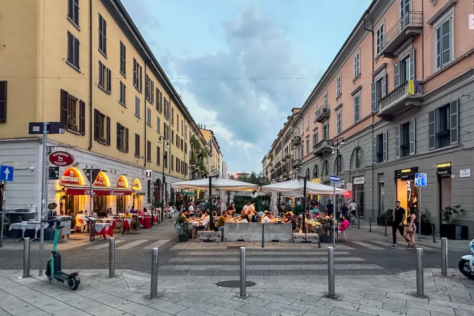 Pedestrianized street in Milan, Italy with outdoor dining tables and umbrellas.